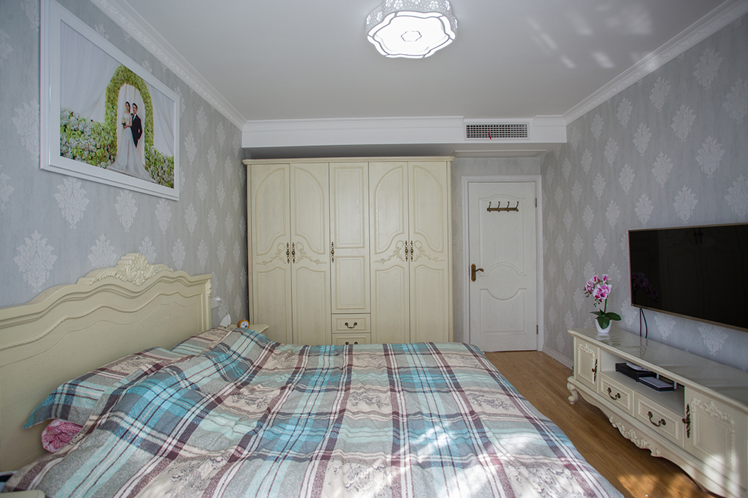 主臥室墻面貼的是淺灰色無紡布，搭配象牙白的整體家具，主臥朝南，陽光照進臥室顯得格外溫馨。
