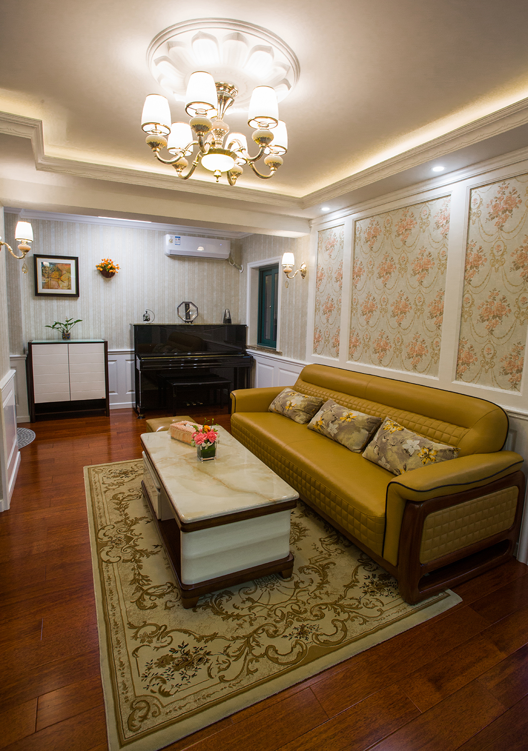 客廳墻面采用白色護(hù)墻板和素雅的墻布搭配，營造出自在、隨意不羈的生活方式，沒有太多造作的修飾與約束，入門的鞋柜黑白搭再配上一抹綠色盆栽，活脫自然，黑色鋼琴應(yīng)眼而入，不經(jīng)意間營造出一種休閑式的浪漫，深色實(shí)木地板搭配黃色地毯和皮質(zhì)沙發(fā)，淺透出一絲奢侈與貴氣，有著新的懷舊、而又不失自在與隨意。

