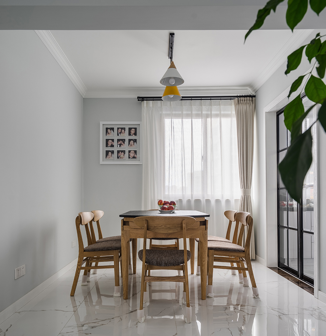 在餐廳的設計上，我們延續了客廳的灰調，明黃色餐廳燈給整個空間多了一絲明快，原木色的餐椅以及深色坐墊現代感分明，淺色窗簾元素中削減了空間的硬度。黑色格子玻璃門與餐廳風格保持協調統一。
