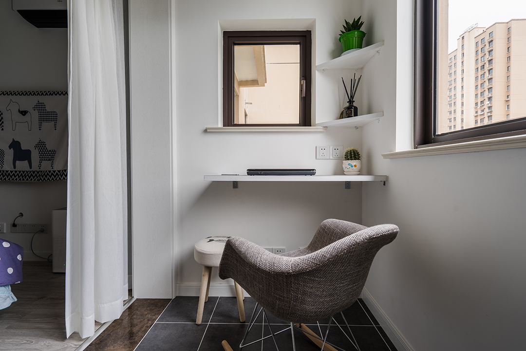 陽臺是主人休閑工作的一個小天地，宜工作宜休閑。白色層板書作書架化繁為簡，實用用且不占用空間。地磚選用灰黑色仿古磚配上白色美縫，再加上布藝小搖椅，好看。