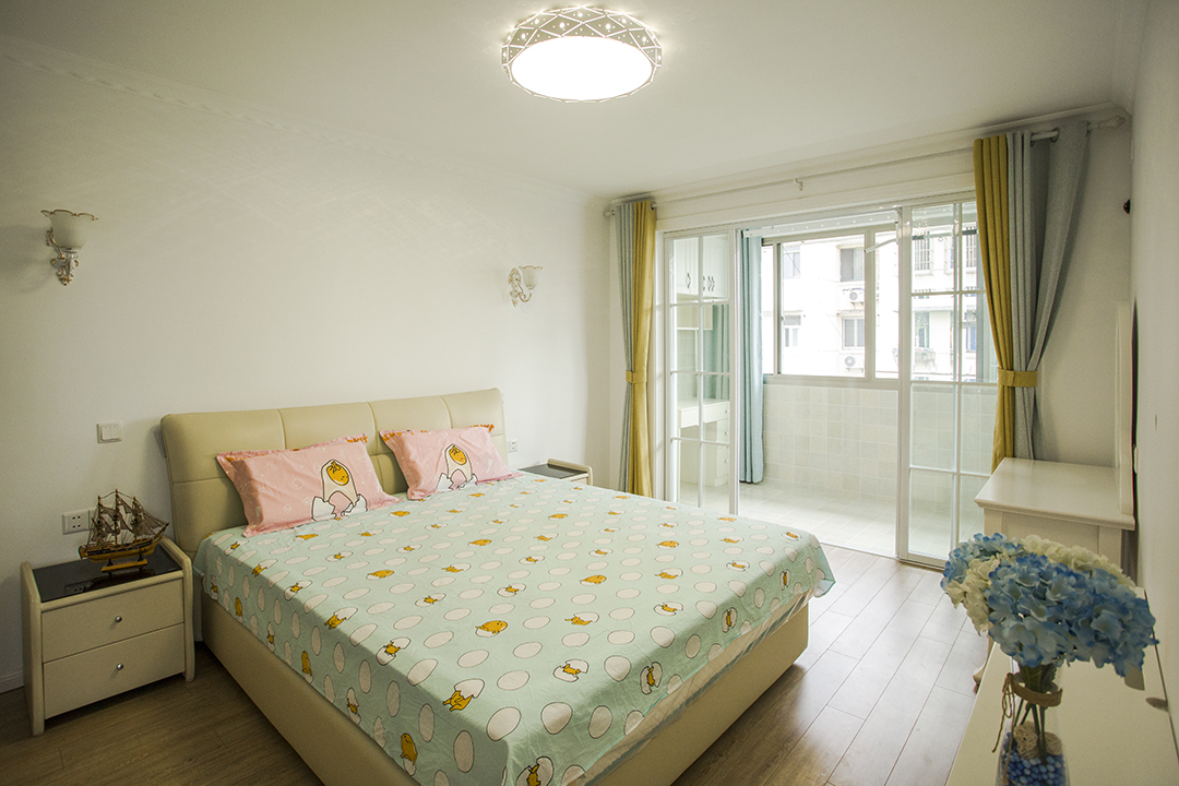 床頭柜上方的壁燈和正中間的吸頂燈各自分工又互相映襯，照亮奢華大氣的軟包雙人床，靜謐安寧。藍白相間的花瓶和精致的梳妝臺似乎都在訴說著主人的幸福和浪漫。
