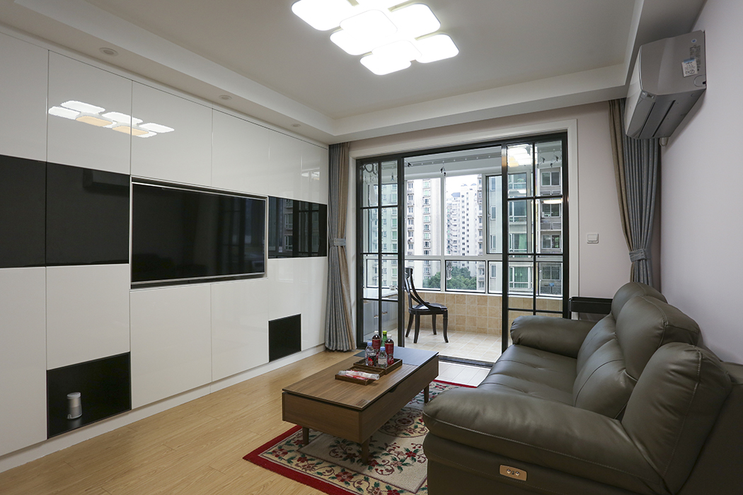 客廳背景墻的設(shè)計(jì)采用整面的亞克力儲(chǔ)物柜作為設(shè)計(jì)方案，黑白的色調(diào)配色簡(jiǎn)潔大氣，搭配淺色的地板人，讓整個(gè)空間整潔而又明亮，陽(yáng)臺(tái)白門套搭配黑格子移門讓整個(gè)空間別具一格。
