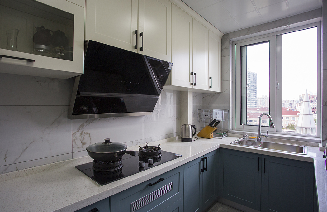 廚房間選擇大理石的玻化磚，再配上模壓門板的櫥柜，上柜以現代簡約里最常見的象牙白為主，下柜以湖藍色的線條門板為主，黑色的門把鎖格外顯眼，起了一定的點綴和裝飾作用，讓整個廚房間更加和諧、時尚。

