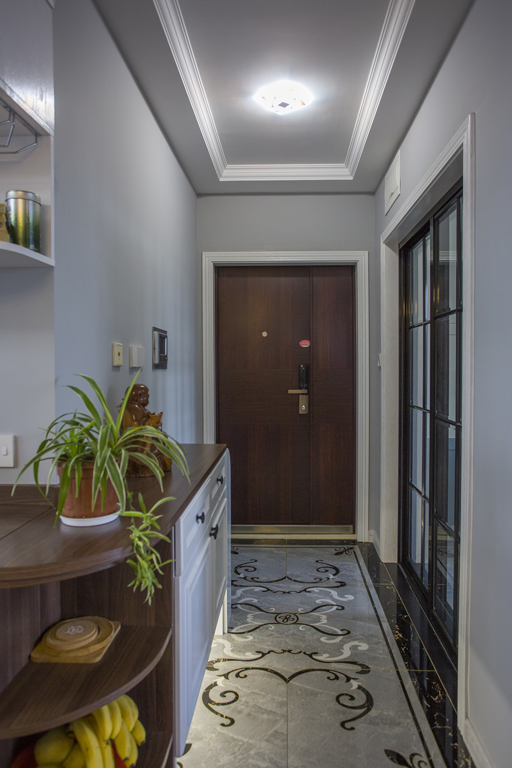 該女業主30多歲，也從事裝飾行業。在工作中，事業有成，追求高品質生活。入戶整體視覺感很長，整體以灰色、黑色和白色相結合，淺灰色瓷磚，再圍繞著一個拼花，讓整體色度更柔和，視覺效果更時尚、大氣，同時在右側加入鞋柜，在出門時能更方便進行儀容的整理，同時也拉寬了視覺效果。