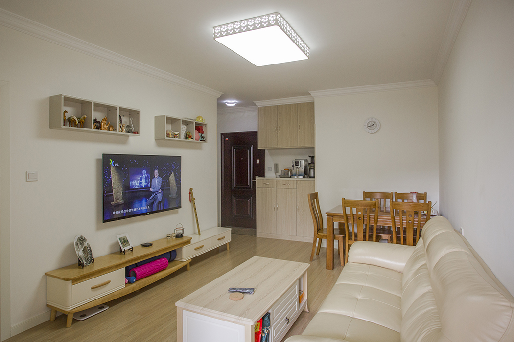 客廳和餐廳于一體，原木色地板和淺黃色墻面互相映襯，清新明亮。電視背景墻是簡易的組合電視柜，再加上裝飾品作點綴，彰顯了主人的品味。
