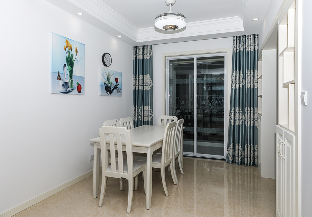  餐廳空間較大，主人事業有成，有收藏愛好，兩個裝飾博古架和裝飾酒柜滿足了收藏需求和對實用功能的要求。米黃色的玻化磚、米白色實木餐桌、白色的頂面造型頂，色調上從淺到深、循序漸進。藍色的裝飾畫、藍色窗簾把餐廳點綴地淋漓盡致。
