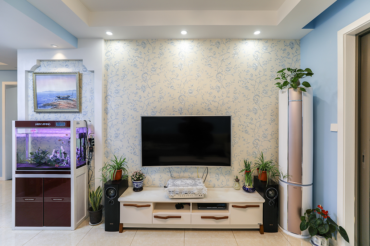 電視背景墻是以白色為底色加藍色小花的墻紙，白色實木低柜突出其線條，與整體風格相融合，旁邊的魚缸為家增添了幾分生氣。 
