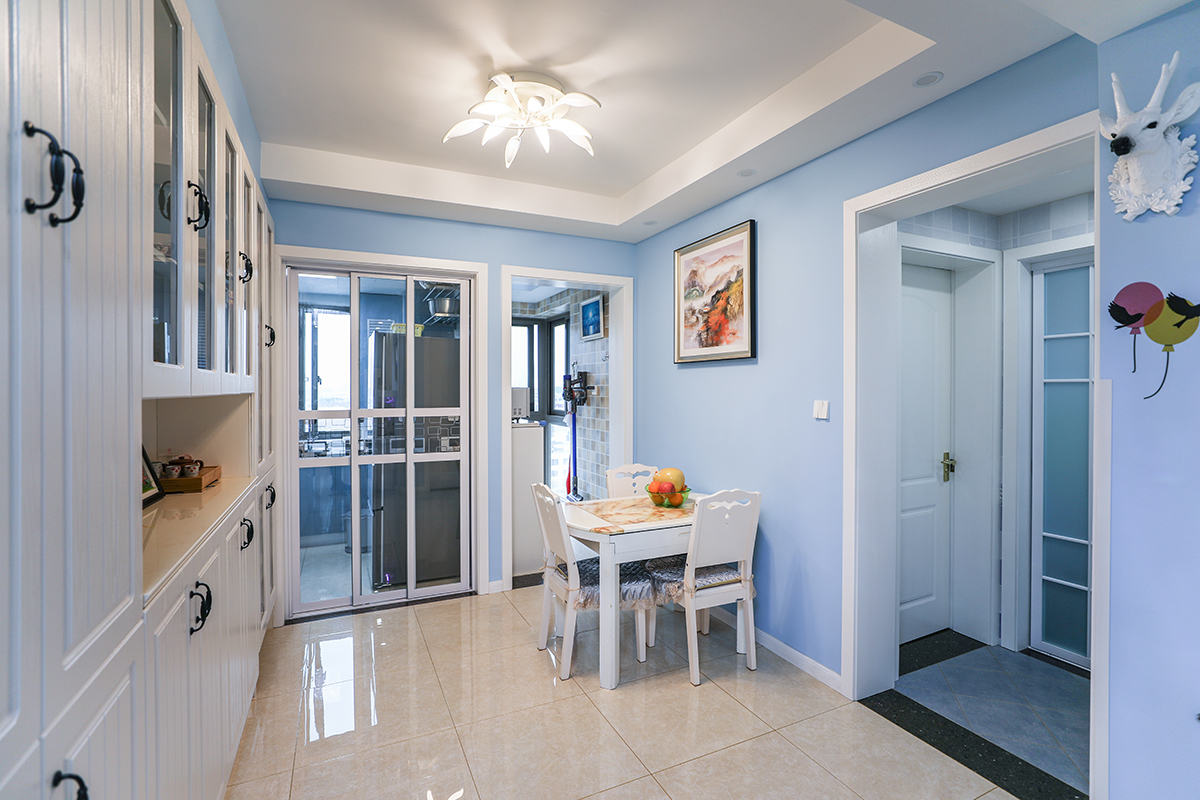 餐廳地面使用淡黃玻化磚，大氣明亮。淡藍色墻面，加上白色的模壓門板酒柜，白色餐桌，還有白色門套，祥和舒適。
