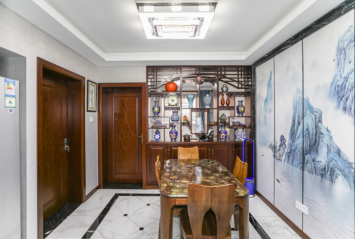 餐廳以黑白灰經典配色外加入了柚木色的中式元素，中式硬包水墨山水畫給與了餐廳另一種靈魂，家里休閑的同時有種隔絕世外的桃源般的生活.中式特有的博古架收藏了主人心愛古董外，又給人一種精致享受的生活方式.
