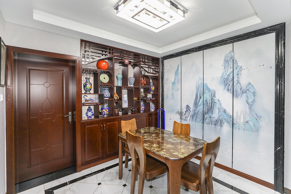 餐廳以黑白灰經典配色外加入了柚木色的中式元素，中式硬包水墨山水畫給與了餐廳另一種靈魂，家里休閑的同時有種隔絕世外的桃源般的生活.中式特有的博古架收藏了主人心愛古董外，又給人一種精致享受的生活方式.
