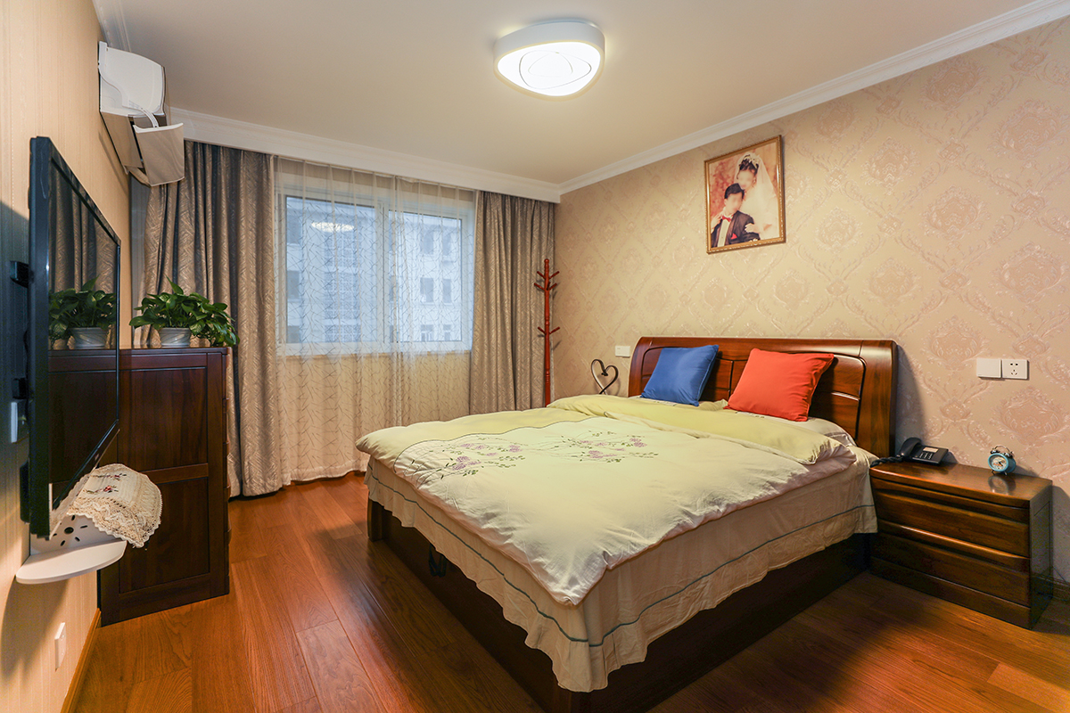 深色地板與實木床互相呼應，墻面做墻紙顯得空間不會單調，頂面石膏線勾勒，同時做窗簾盒，隱藏了窗簾軌道，使得空間更為簡潔大方。
