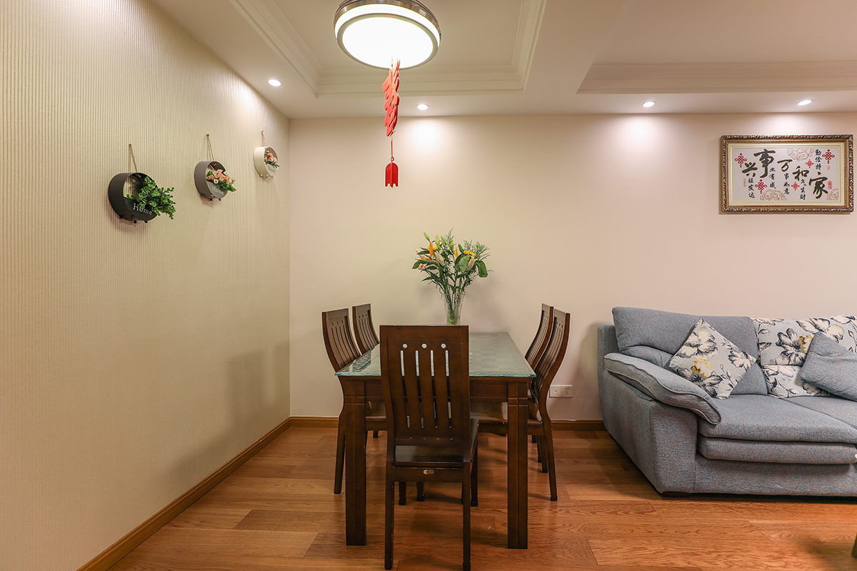 白色的墻體深色的桌子藍色的布藝沙發加以墻面的綠植裝飾，沉穩又不單調。沙發背景是女主人手工刺繡的家和萬事興，使得整體氛圍溫馨。
