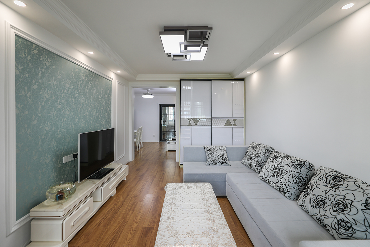 該套房客廳是由原來(lái)的臥室改造而成，光線不太明亮，所以整體以白色為主，配上灰色的沙發(fā)，現(xiàn)代時(shí)尚的吸頂燈，使空間干凈清爽、豐富多彩，不單一呆板。
