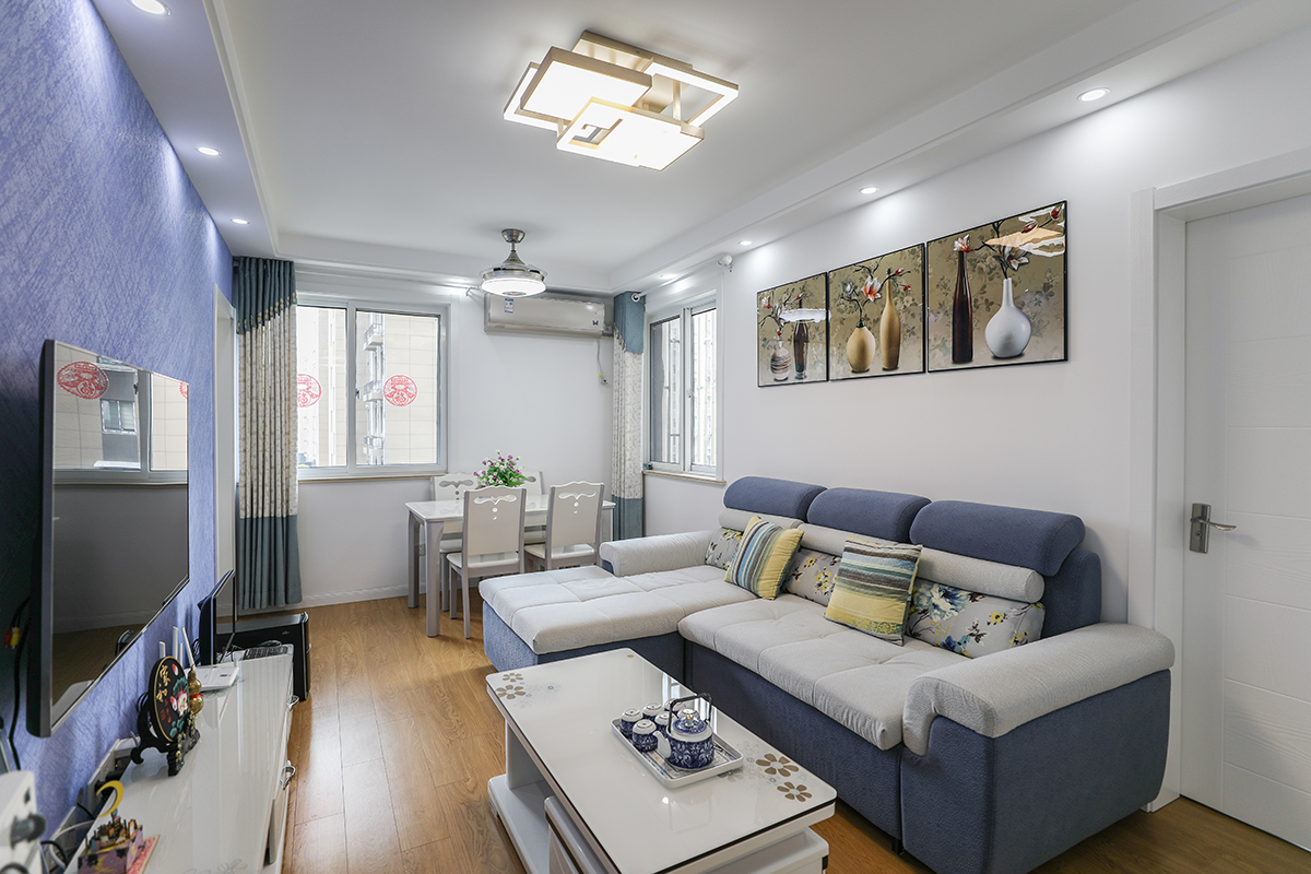 客廳的布置簡約而不簡單，溫暖而不奢華。電視柜和茶幾的顏色運用了皓白色，再搭配上藍白色組合式沙發，原木色的地板，既有現代簡約風格的時尚也少了幾分冰冷之感。而墻面上掛著三幅陶瓷組畫，既增加了客廳的情調，也能來看出主人的生活品味。
