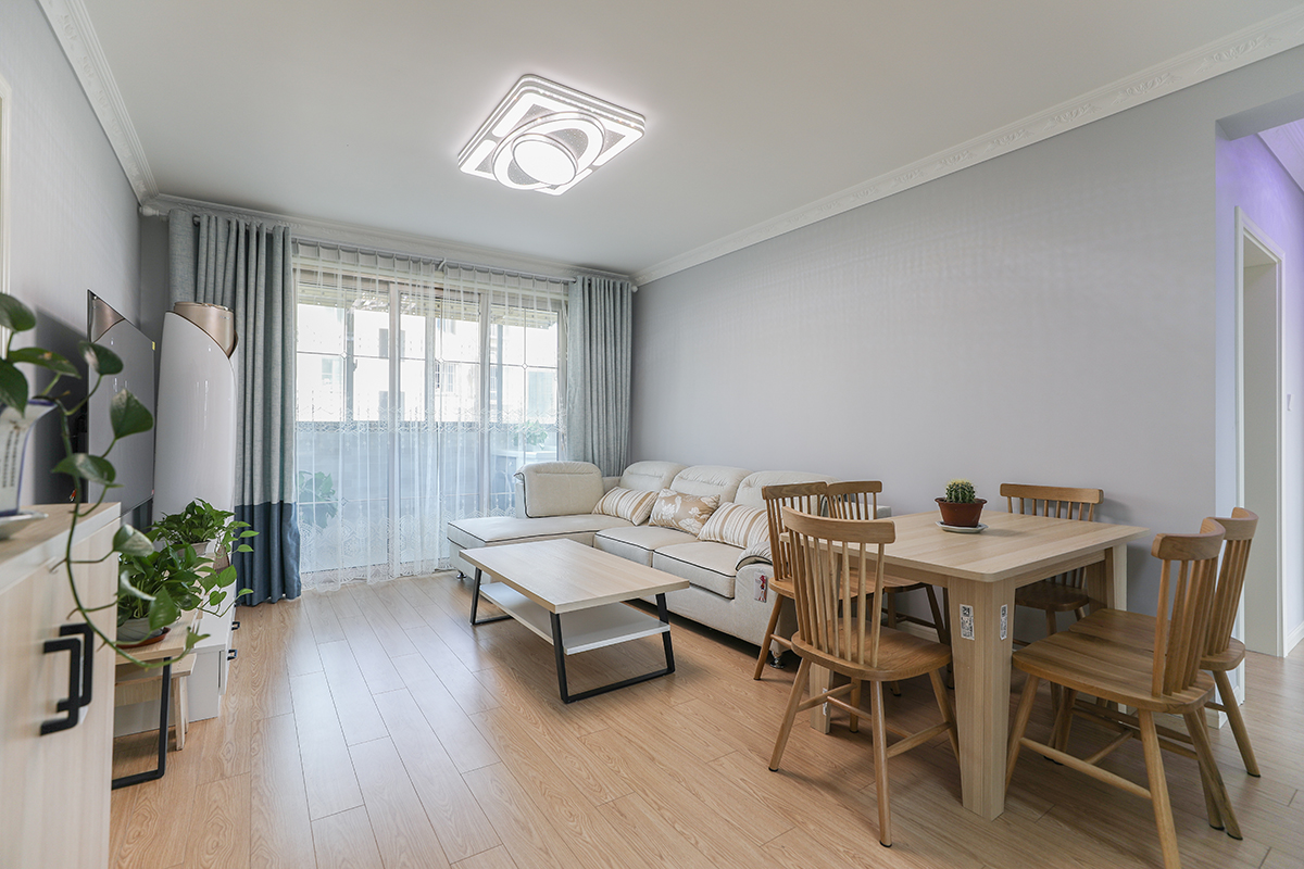 客廳整體墻面選用淺灰色，頂面走歐式石膏線，與簡(jiǎn)歐踢腳線做上下呼應(yīng)，簡(jiǎn)單而不單調(diào)。軟裝方面，灰藍(lán)色的窗簾與墻面裝飾畫(huà)相近色的色彩運(yùn)用，凸顯層次感。用白色的布藝沙發(fā)與灰色墻面交相呼應(yīng)溫馨而不突兀。暖色的地板及原木的桌椅中和掉整個(gè)空間的冷意。
