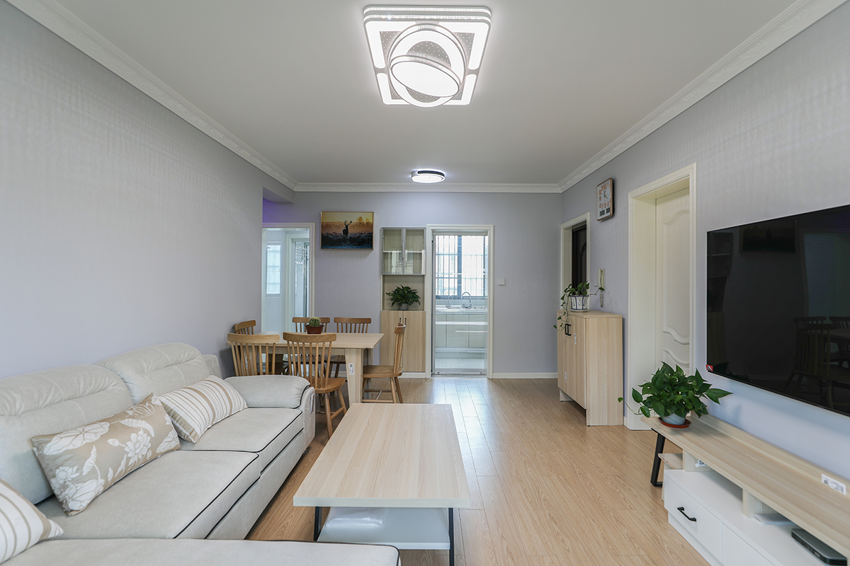 客廳整體墻面選用淺灰色，頂面走歐式石膏線，與簡(jiǎn)歐踢腳線做上下呼應(yīng)，簡(jiǎn)單而不單調(diào)。軟裝方面，灰藍(lán)色的窗簾與墻面裝飾畫(huà)相近色的色彩運(yùn)用，凸顯層次感。用白色的布藝沙發(fā)與灰色墻面交相呼應(yīng)溫馨而不突兀。暖色的地板及原木的桌椅中和掉整個(gè)空間的冷意。
