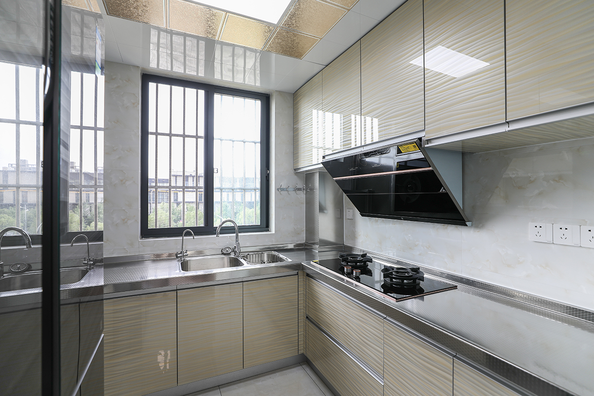 廚房臺(tái)面選用304不銹鋼，與不銹鋼水槽焊接一體，方便清潔打理。整個(gè)空間顯得明亮。廚房櫥柜門(mén)板選用波浪紋亞克力門(mén)板。暖色調(diào)的運(yùn)用中和了臺(tái)面的冰冷。
