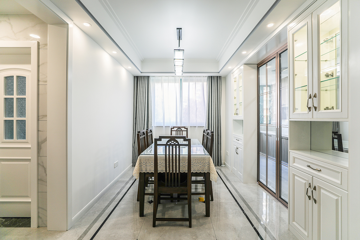 餐廳空間較大，主人事業有成，有收藏愛好，兩個裝飾酒柜滿足了收藏需求和對實用功能的要求。白色的玻化磚、深色實木餐桌、白色的頂面造型頂，色調上從淺到深、循序漸進。藍灰色窗簾把餐廳點綴地淋漓盡致。
