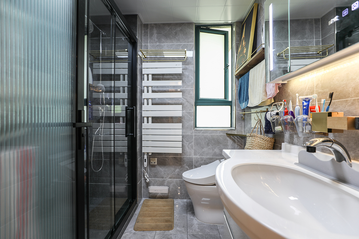 衛(wèi)生間灰色瓷磚，白色的潔具搭配黑色邊框的淋浴房永遠是那么的經典，電加熱毛巾架的使用也是非常的貼心，在寒冷的冬天給人一絲絲的暖意。