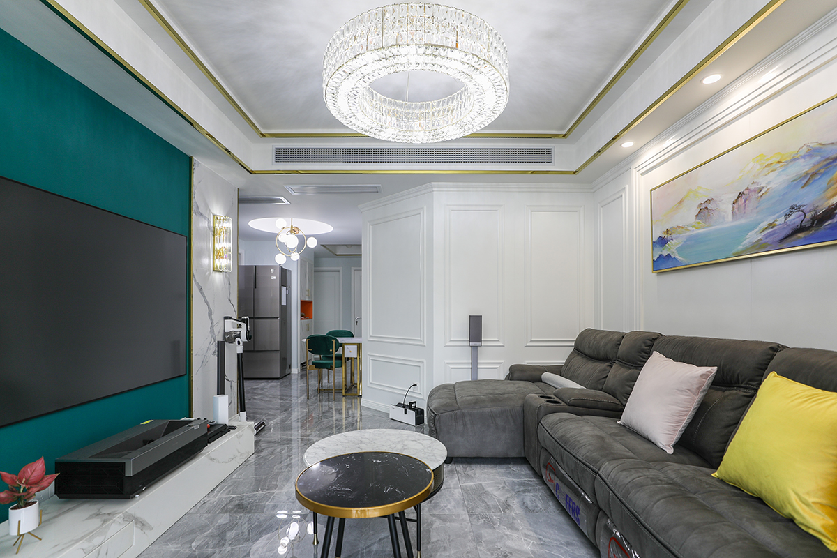 客廳整體風(fēng)格采用木，鏡，沙風(fēng)格，是當(dāng)下比較時尚也是板式的處理方式，在顏色上做了調(diào)色，配上精致的玻璃燈和線簾的裝飾，把板式的硬線條做了軟性富有穩(wěn)重。黑色的皮沙發(fā)，配上灰色的地磚，有層次感的護墻板，更彰顯出了整體的效果。電視背景墻，采用輕奢通用的爵士白上墻，再配上不銹鋼線條，中間是墨綠色的墻紙，細節(jié)附金色系裝飾點綴，時尚大氣。客廳的茶幾和電視背景墻的大理石相呼應(yīng)，茶幾側(cè)面的鏡色玻璃和茶幾的金屬線條。窗簾上的檸檬黃，和沙發(fā)上的檸檬黃抱枕相呼應(yīng)。客廳頂上的水晶燈，配上輕奢的金屬鋼線條搭在一起，使家里輕奢的效果更沉穩(wěn)。紅色的綠植在灰、綠、金屬鋼線條之前，作為點綴。
