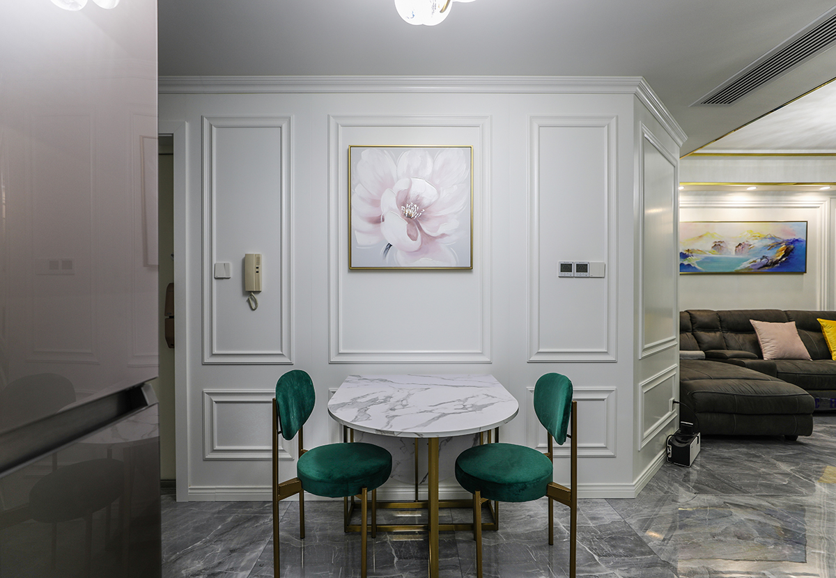 餐桌的那面墻，配上白色的護墻板，中間掛了一副粉色的掛畫，配上有金屬線條的邊框，跟客廳的效果相呼應(yīng)，墨綠色的桌椅，大理石的桌面，帶有金屬線條的桌角，使得客廳和餐廳更諧、穩(wěn)重、時尚、大氣。
