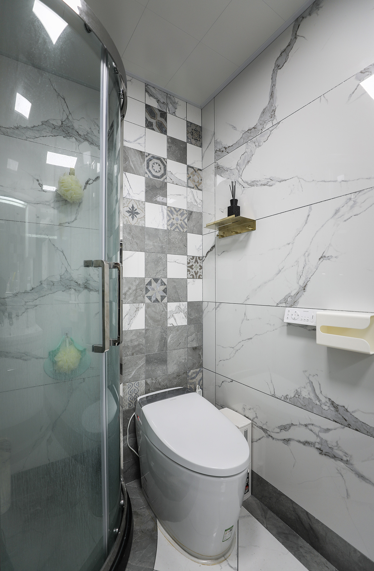 衛(wèi)生間利用黑白灰相間的微晶石磚，把整體的效果凸顯的更卓著。馬桶的背景墻采用小方格的圖案，配有灰色的大理石，把功能和區(qū)域性分開的更明顯。馬桶的另外三面大理石墻面，跟客廳的背景墻、茶幾的茶桌、鞋柜的門板，互相呼應(yīng)。再配上金屬的線條，帶著輕奢元素和現(xiàn)代材質(zhì)的組合展現(xiàn)，讓整套效果品質(zhì)不落俗套。
