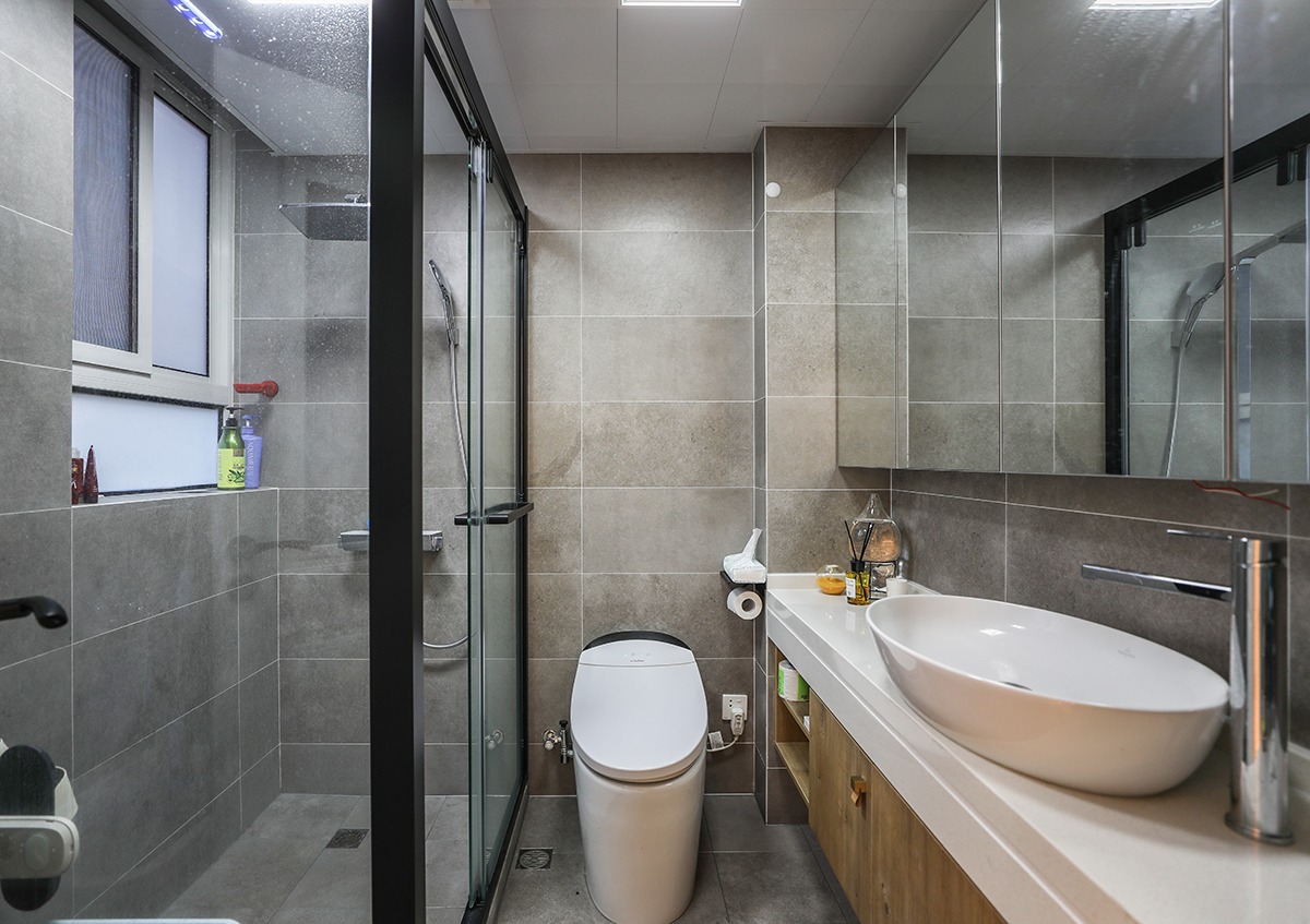 這個衛生間整體格局非常的不錯，所以在墻面瓷磚上的運用采用了整體灰色系風格搭配，主要以灰色磚為主，加以木翁色的洗臉柜，使得整體的色彩非常的舒適協調。
