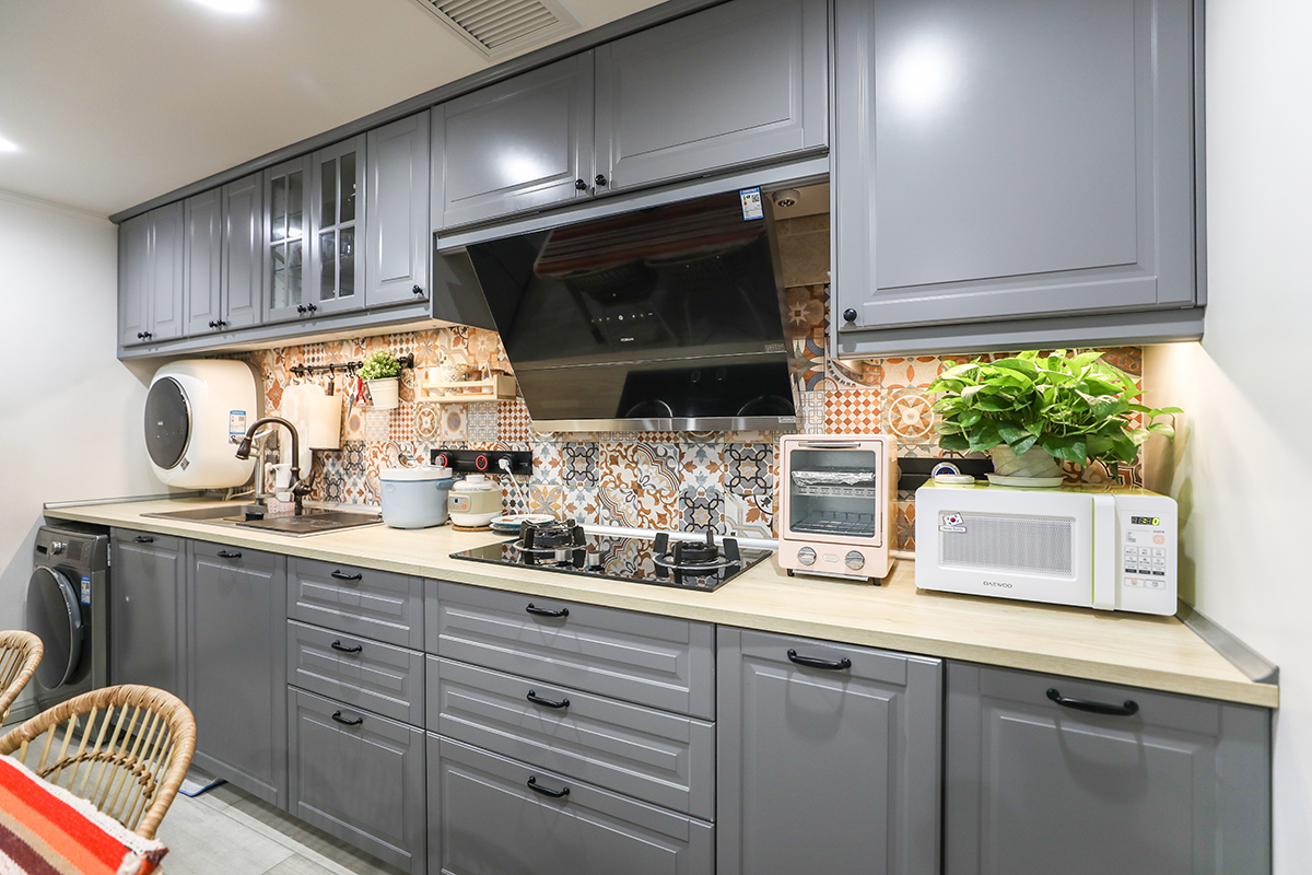 廚房區域選用模壓板櫥柜，臺面沒用選用傳統的石英石臺面或是不銹鋼臺面。而是選用了三氯氰胺樹脂板做臺面，提升了整個空間的溫度。花磚做背景，即使臺面堆放物品再多也不會顯得空間凌亂。由于衛生間空間較小，所以櫥柜做了內嵌洗衣機柜及掛壁式洗衣機。形成一個多功能空間。
