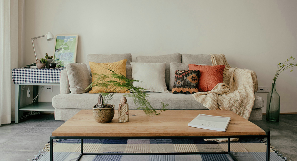 客廳空間開闊明亮。利用淺色紗幔窗簾優化自然光的吸采，讓空間擁有足夠的恬靜感。業主對日式風格很喜歡，客廳的茶幾是業主在日本旅游時帶回國。灰色的布藝沙發，沉穩大氣，搭配自然紋理的原木茶幾和座椅，讓濃郁的日式風情填滿整個空間。柔軟舒適的沙發，隨意擺放著幾個抱枕，再增加一張橙色的真皮單人椅，無形之中提升了空間的質感。
