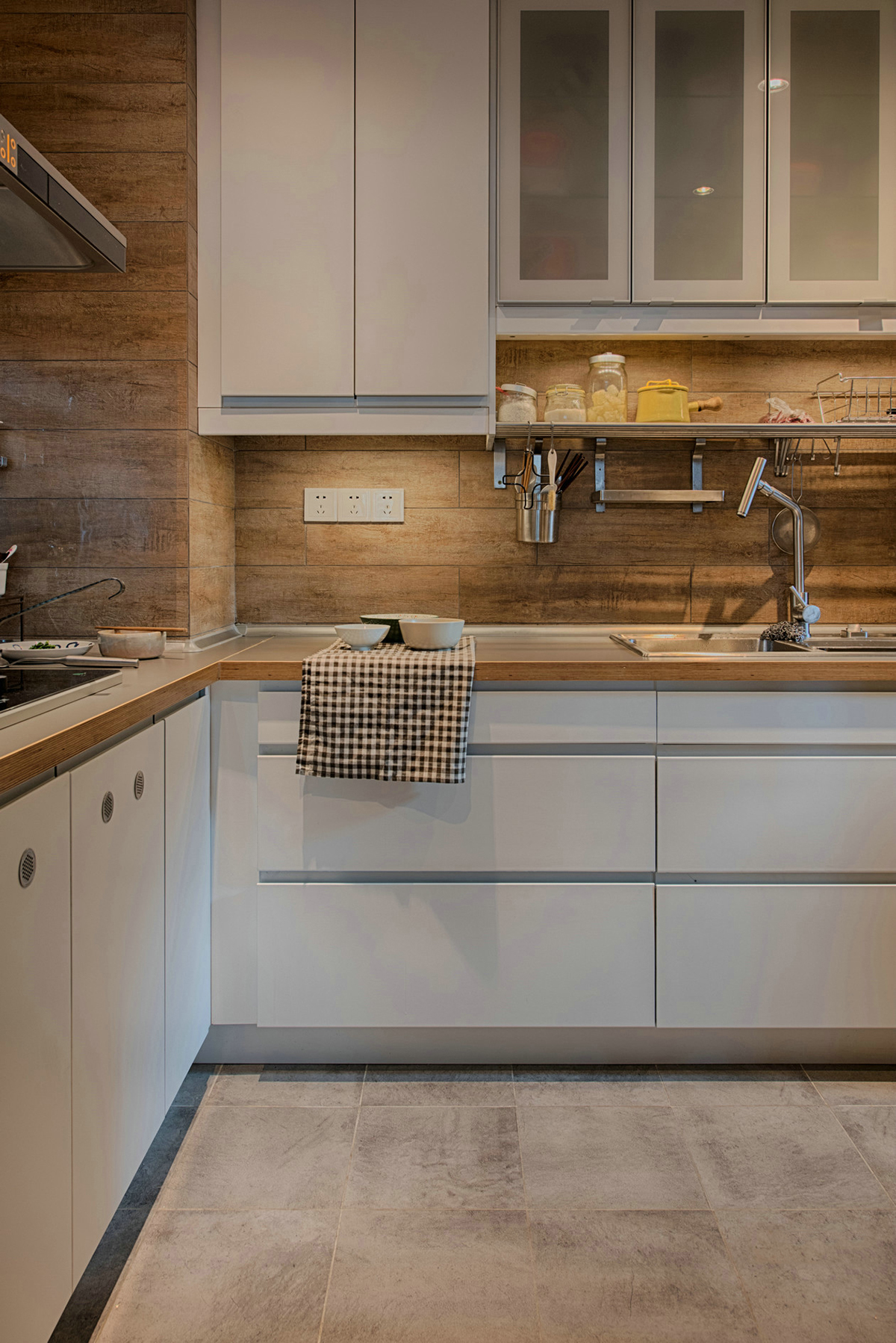 廚房清新雅致，追求整潔和舒適。不銹鋼臺面，低調不張揚，干凈明亮。深木色系墻磚，原木的韻味，讓廚房也能散發出自然氣息。業主愛旅游、愛收藏、愛養花弄草，因此在空間利用中，設計師為他們打造了一間多功能茶室，原木的小桌子，擺放著精致的茶具，讓他們在這里喝茶、看書、賞花，享受閑暇時光。
