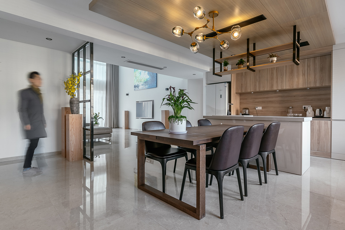 木飾面是貫穿整個空間的，顏色層次是黑白灰+木色的基調。大面積白色會使空間沒有很冷，所以用木色的溫潤來調節整個空間溫度。讓家的感覺更溫馨。櫥柜與頂面不是一家生產，在施工中先確定了櫥柜顏色。帶著樣板去定制頂面顏色，整體效果基本一致。櫥柜和吧臺的位置就是原來的空中花園，打通后空間開闊，可以和客廳統一。為了配合整體簡潔干凈的感覺，窗簾我選用木色百葉窗。透光和隱私性和布藝窗簾同等。右側的廚房是紅橡制作，為了保證實木的本質只做了清漆。顏色質感是市場銷售產品所達不到的。
